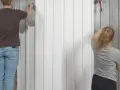 Man och kvinna målar fasad med roller. De arbetar sida vid sida för att ge huset ett nytt utseende.