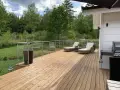 Nyligen oljad altan med solstolar och grill. Vacker utsikt över grönskande skog och en sommarhimmel.