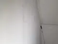 En lång skrapa med handtag står lutad mot en nyspacklad vägg, redo att slipa spackel för en slät yta.