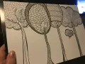 En hand håller ett papper med en detaljerad doodle av fantasifulla träd. Varje träd har unika mönster i kronorna, som om någon ville skapa doodle-konst.