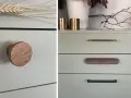 Detaljer från en målad byrå med olika handtag: ett runt i trä, ett mässingshandtag och ett avlångt i trä.