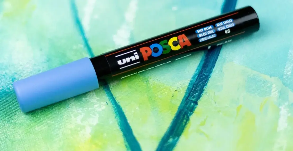 En ljusblå Posca-tuschpenna ligger på en abstrakt målning i gröna och blå nyanser. Perfekt för att måla med tuschpennor.