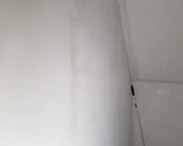En lång skrapa med handtag står lutad mot en nyspacklad vägg, redo att slipa spackel för en slät yta.