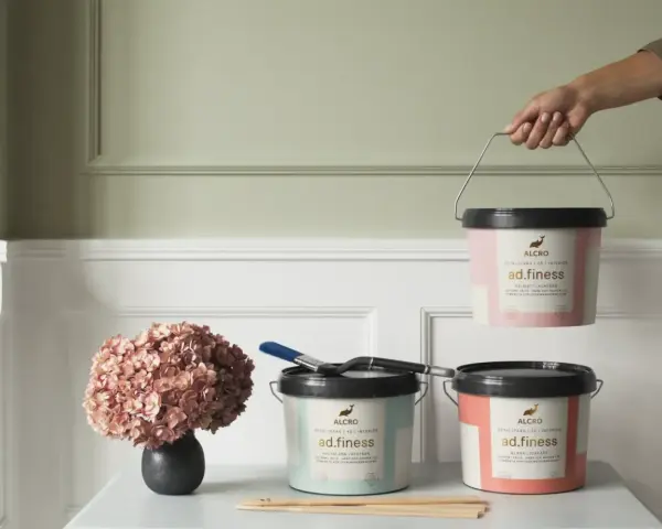 Tre burkar Alcro ad.finess färg i olika kulörer. En burk lyfts, en med pensel och en med en hortensia. Välj mellan sidenmatt vs matt för ditt projekt.