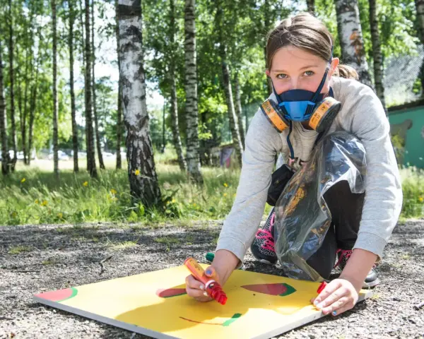Ung flicka med munskydd skapar graffiti på papper utomhus.