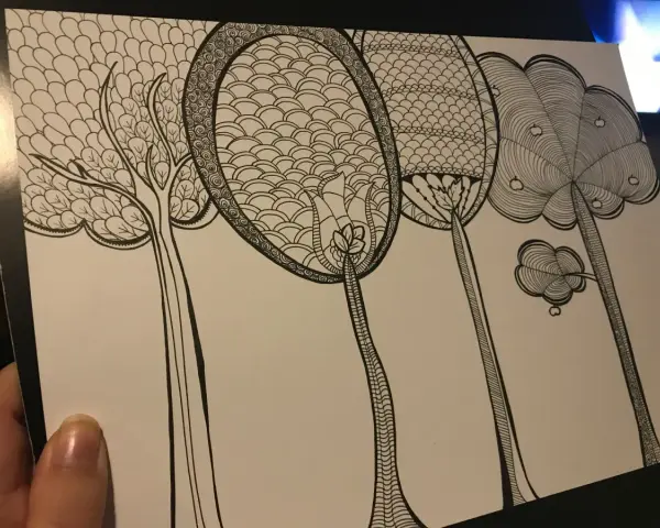 En hand håller ett papper med en detaljerad doodle av fantasifulla träd. Varje träd har unika mönster i kronorna, som om någon ville skapa doodle-konst.