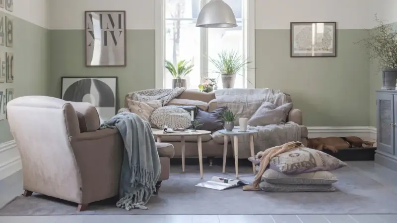 Vardagsrum i svensk stil med bekväm soffa, fåtölj och en sovande hund. Vårljus strömmar in genom fönstret och skapar en mysig atmosfär.